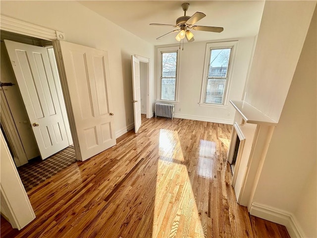 unfurnished living room featuring ceiling fan, radiator, and light hardwood / wood-style floors