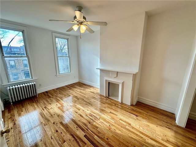 unfurnished living room featuring baseboards, ceiling fan, radiator heating unit, and hardwood / wood-style flooring