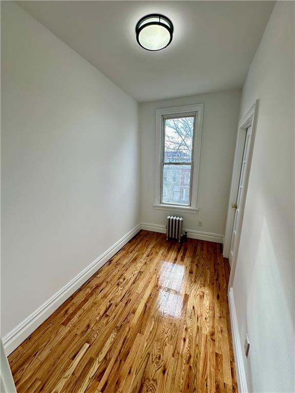 unfurnished bedroom with light wood-type flooring, radiator, and baseboards