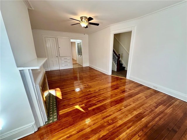 unfurnished room with ceiling fan, baseboards, stairs, ornamental molding, and wood-type flooring