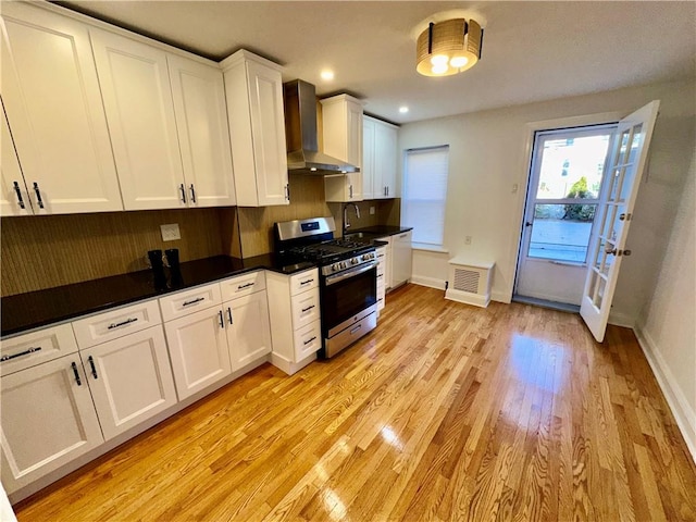 kitchen featuring white cabinets, wall chimney range hood, light wood-type flooring, gas stove, and dark countertops