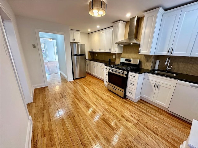 kitchen with white cabinets, wall chimney exhaust hood, light wood-style flooring, stainless steel appliances, and backsplash