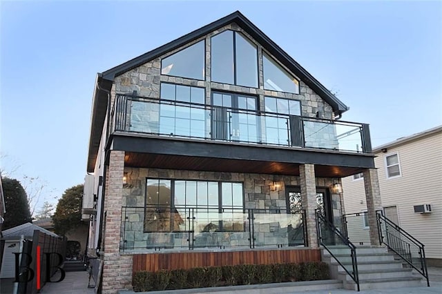 contemporary house with stone siding, covered porch, and a balcony