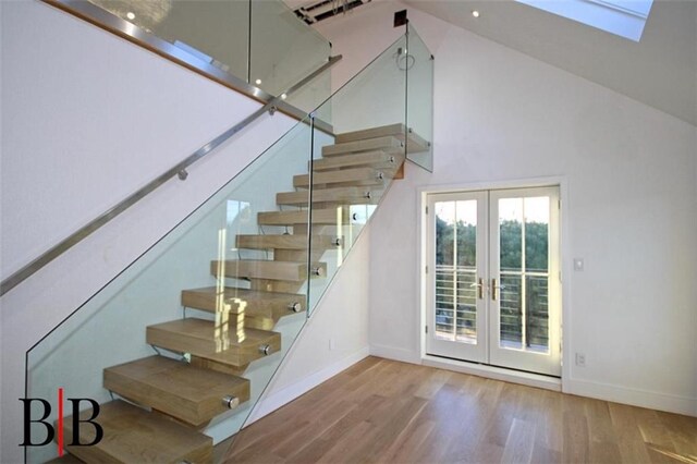 staircase featuring baseboards, french doors, a skylight, wood finished floors, and high vaulted ceiling