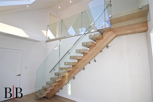 stairs with baseboards, high vaulted ceiling, and wood finished floors