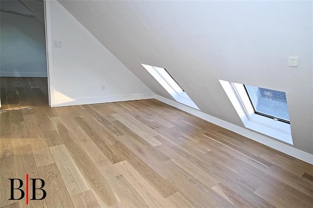 additional living space with baseboards, vaulted ceiling with skylight, and wood finished floors