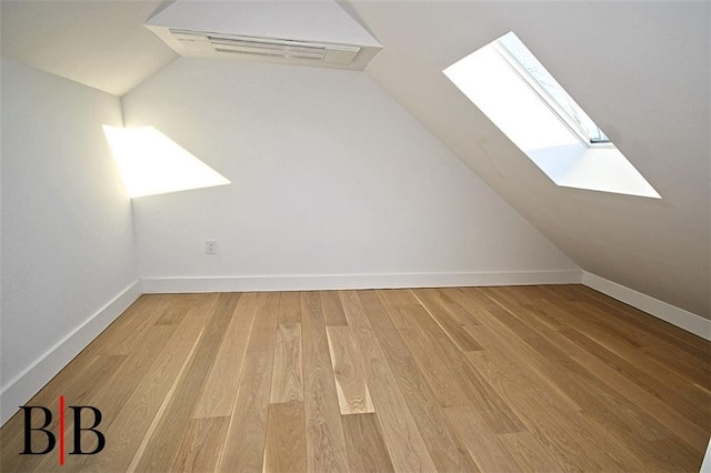 bonus room featuring vaulted ceiling with skylight, light wood-style flooring, and baseboards