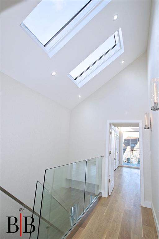 hallway featuring recessed lighting, light wood-style flooring, high vaulted ceiling, and a skylight