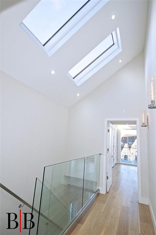 hallway featuring a skylight, high vaulted ceiling, recessed lighting, and light wood-type flooring
