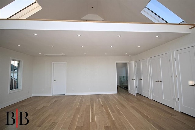 interior space featuring recessed lighting, baseboards, lofted ceiling with skylight, and light wood finished floors