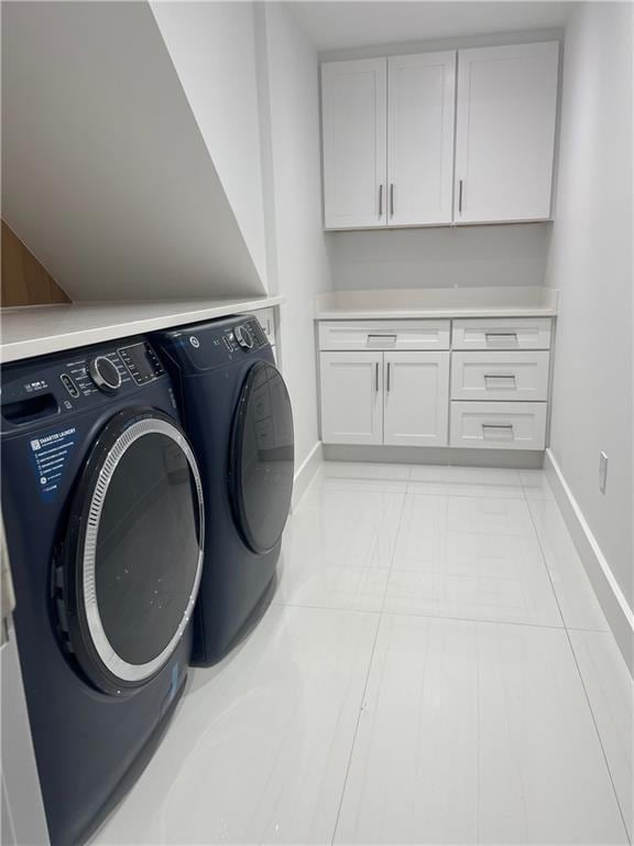 clothes washing area featuring light tile patterned floors, baseboards, cabinet space, and washing machine and clothes dryer