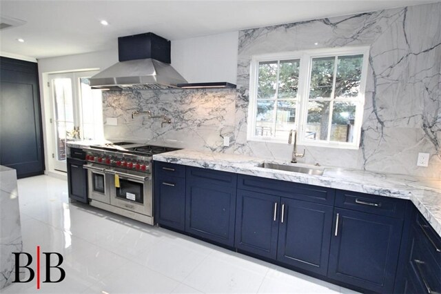 kitchen with island range hood, range with two ovens, blue cabinets, light stone counters, and sink