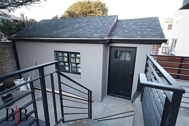 doorway to property with roof with shingles and stucco siding