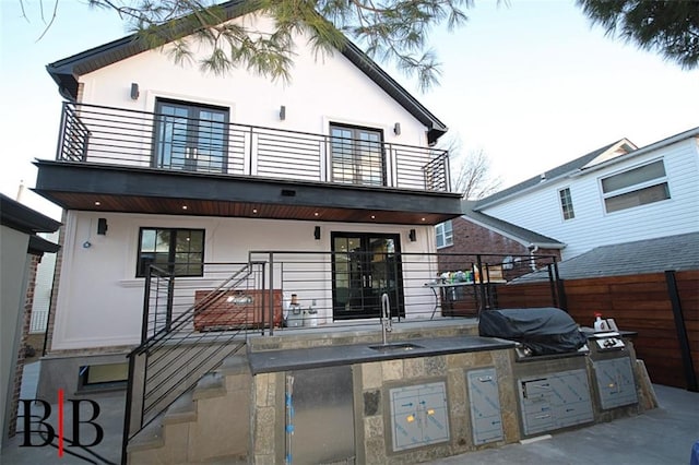 rear view of property featuring a sink, stucco siding, and fence