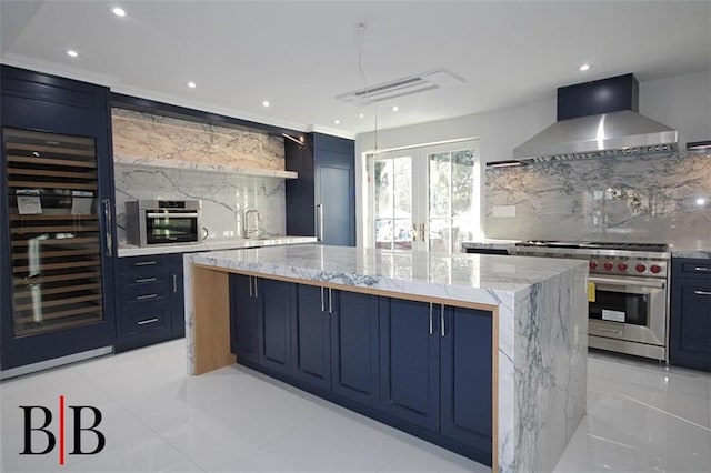 kitchen featuring blue cabinets, light stone counters, a spacious island, stainless steel appliances, and wall chimney range hood