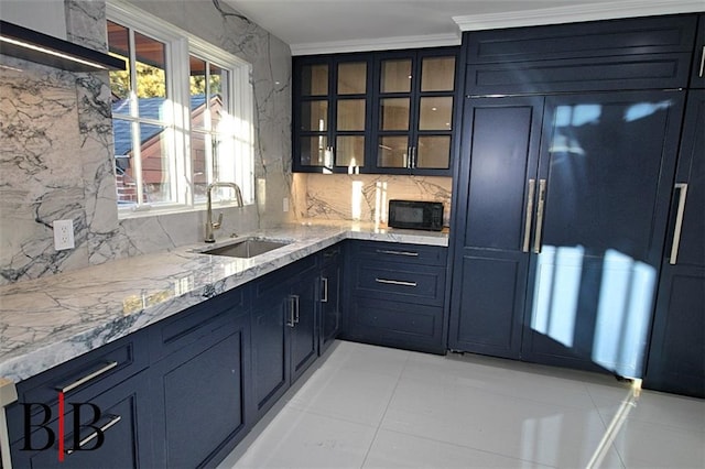 kitchen featuring light stone counters, glass insert cabinets, tasteful backsplash, and a sink