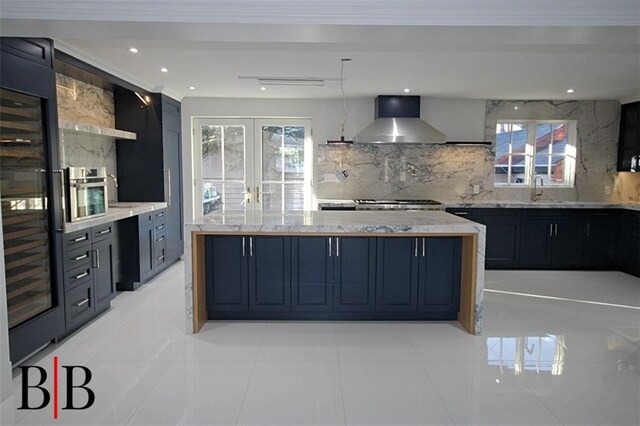 kitchen featuring backsplash, oven, crown molding, a large island, and wall chimney exhaust hood