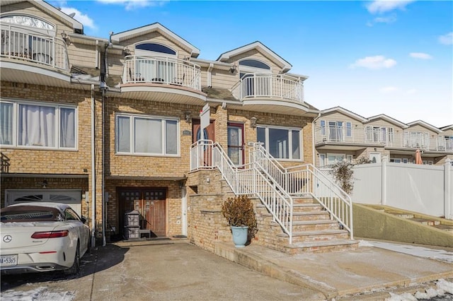 view of property with a garage, concrete driveway, a balcony, fence, and brick siding