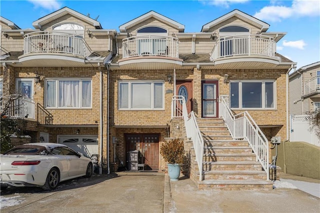 multi unit property with a garage, a balcony, concrete driveway, and brick siding