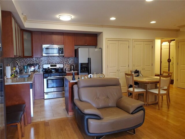 kitchen featuring appliances with stainless steel finishes, light wood-type flooring, light stone counters, decorative backsplash, and sink