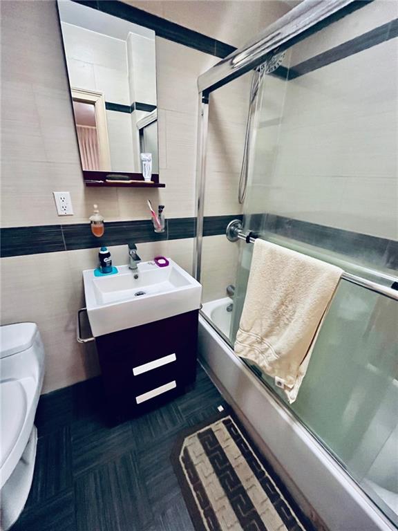 full bathroom with toilet, combined bath / shower with glass door, tile walls, and vanity