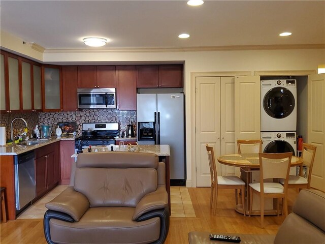 kitchen featuring sink, ornamental molding, light stone countertops, stacked washer and dryer, and appliances with stainless steel finishes