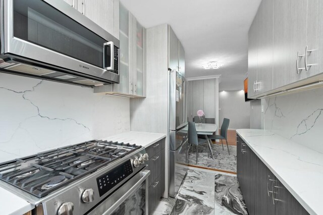 kitchen with decorative backsplash, appliances with stainless steel finishes, gray cabinets, and light stone countertops