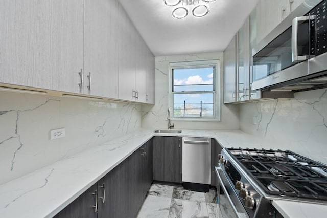 kitchen with light stone countertops, appliances with stainless steel finishes, sink, and backsplash