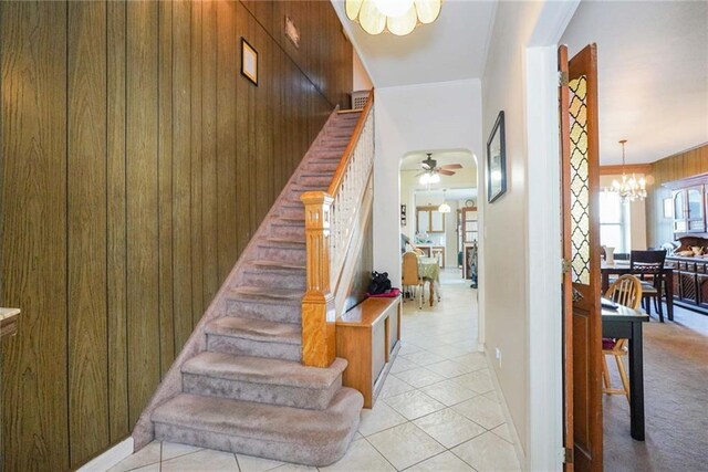 stairway with ceiling fan with notable chandelier, wood walls, and tile patterned flooring