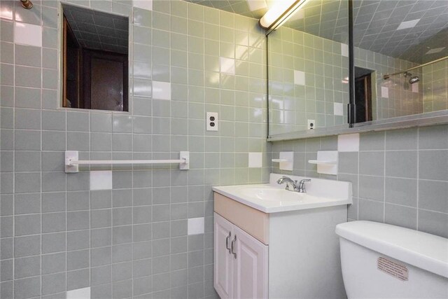 bathroom with toilet, vanity, tile walls, and a shower