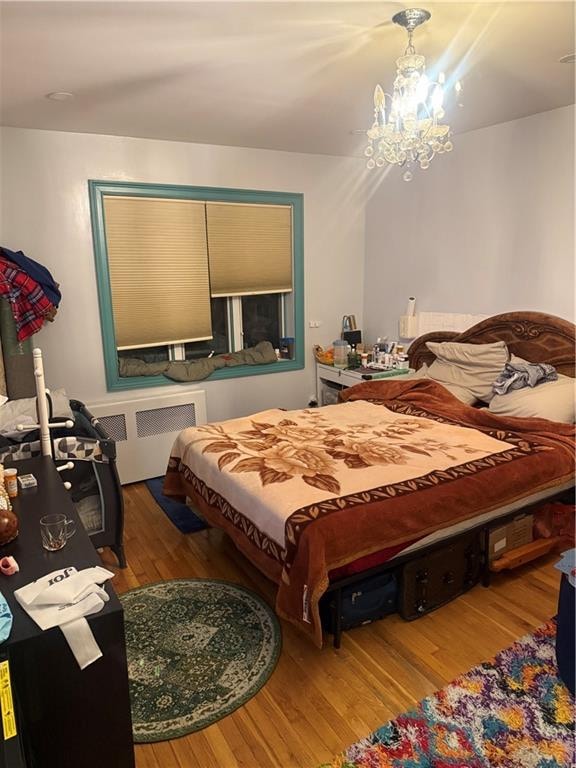 bedroom featuring an inviting chandelier, radiator heating unit, and wood finished floors