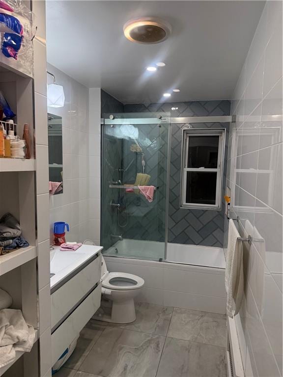 bathroom featuring toilet, shower / bath combination with glass door, tile walls, and vanity