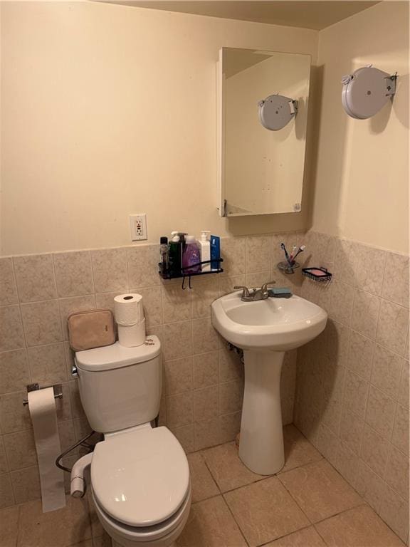 half bath featuring tile patterned flooring, a wainscoted wall, tile walls, and toilet