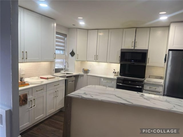 kitchen featuring light stone counters, stainless steel appliances, a sink, backsplash, and dark wood-style floors