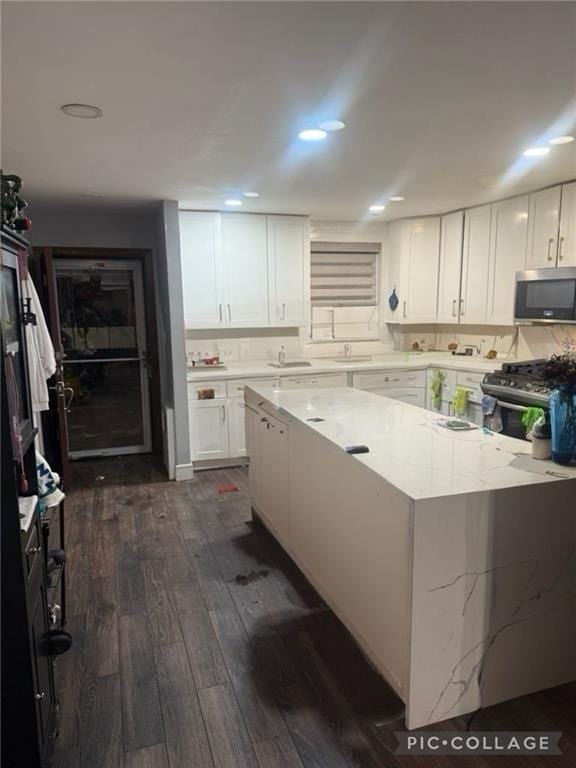 kitchen featuring dark wood-style floors, light stone counters, appliances with stainless steel finishes, and white cabinetry