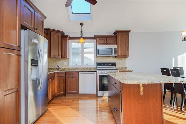 kitchen with a breakfast bar area, a center island, hanging light fixtures, stainless steel appliances, and light wood-type flooring