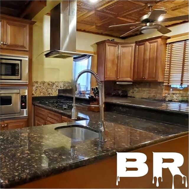 kitchen with stainless steel appliances, island exhaust hood, dark stone counters, ceiling fan, and sink