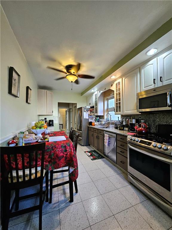 kitchen featuring stainless steel appliances, sink, white cabinetry, ceiling fan, and decorative backsplash