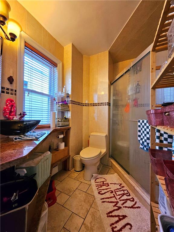 bathroom featuring toilet, tile patterned flooring, tile walls, and walk in shower