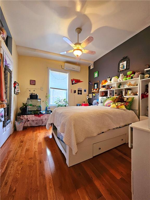 bedroom featuring wood-type flooring, an AC wall unit, and ceiling fan