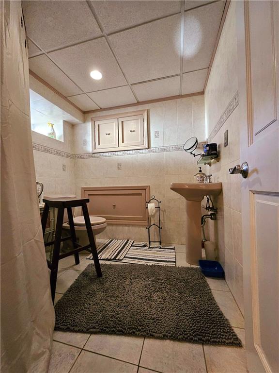 bathroom with tile walls, tile patterned flooring, toilet, and a drop ceiling