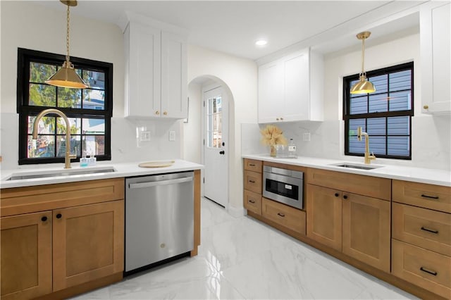 kitchen featuring stainless steel dishwasher, white cabinets, decorative light fixtures, and sink