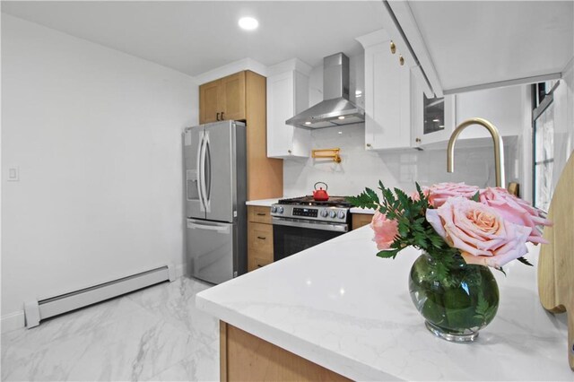 kitchen featuring a baseboard radiator, white cabinets, appliances with stainless steel finishes, wall chimney range hood, and light stone counters