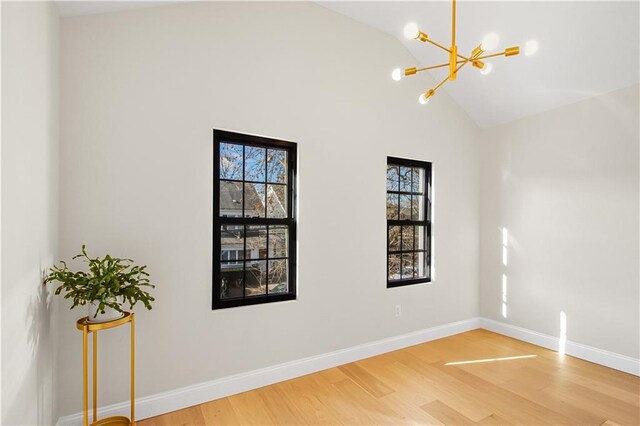 empty room with hardwood / wood-style flooring, a wealth of natural light, high vaulted ceiling, and a chandelier