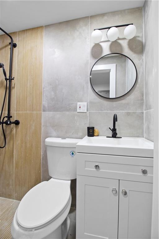 bathroom with toilet, a shower, decorative backsplash, tile walls, and vanity