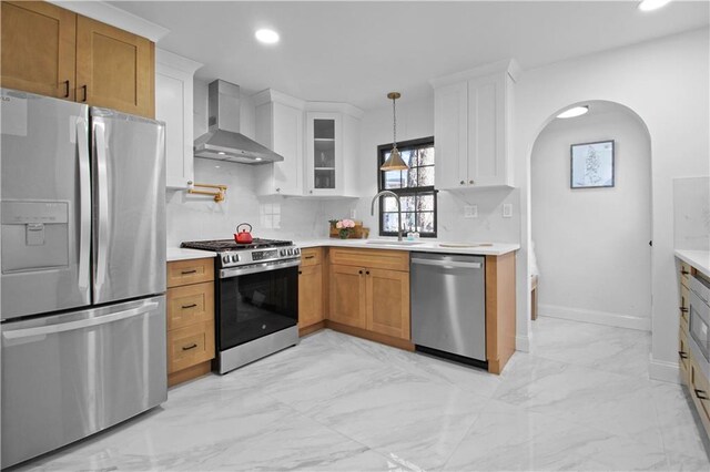 kitchen with appliances with stainless steel finishes, sink, white cabinets, and wall chimney range hood