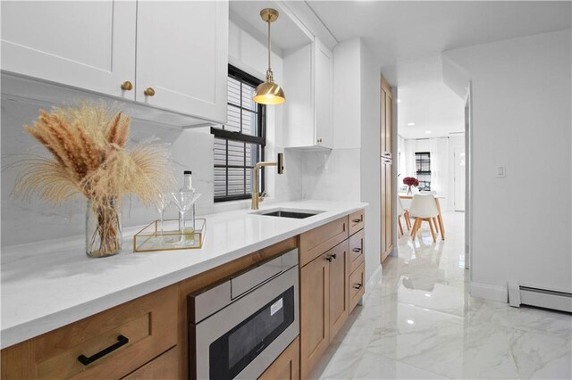 kitchen with stainless steel microwave, sink, hanging light fixtures, white cabinets, and a baseboard radiator