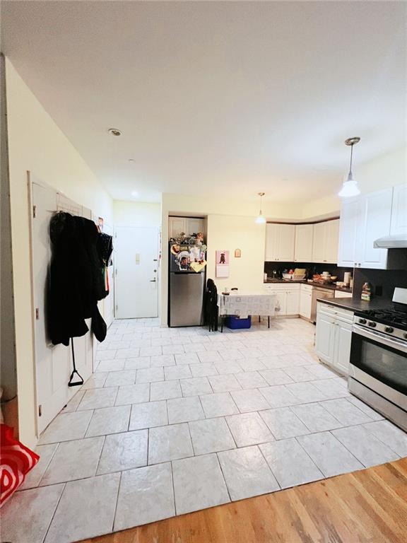 kitchen with appliances with stainless steel finishes, hanging light fixtures, white cabinets, light tile patterned flooring, and tasteful backsplash