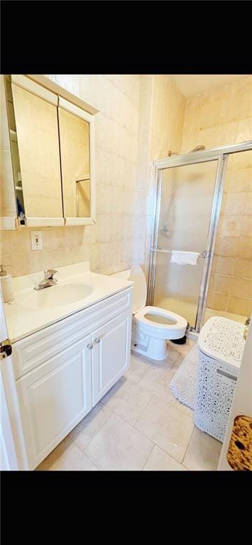 bathroom with toilet, tile patterned flooring, tile walls, an enclosed shower, and vanity