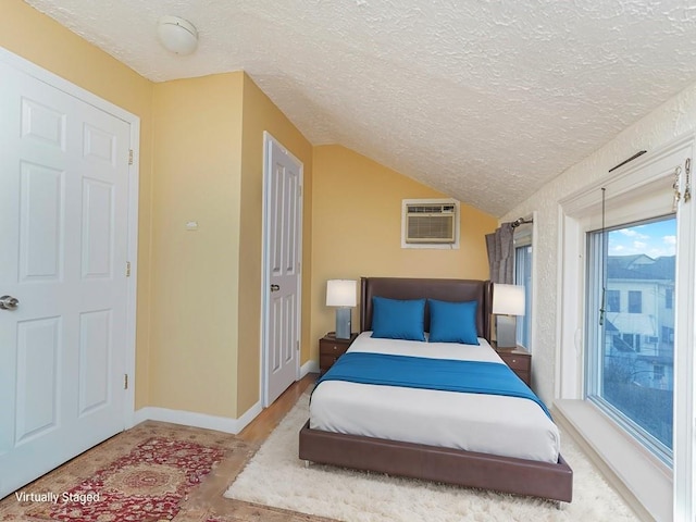 bedroom with vaulted ceiling, access to outside, a wall mounted AC, and a textured ceiling